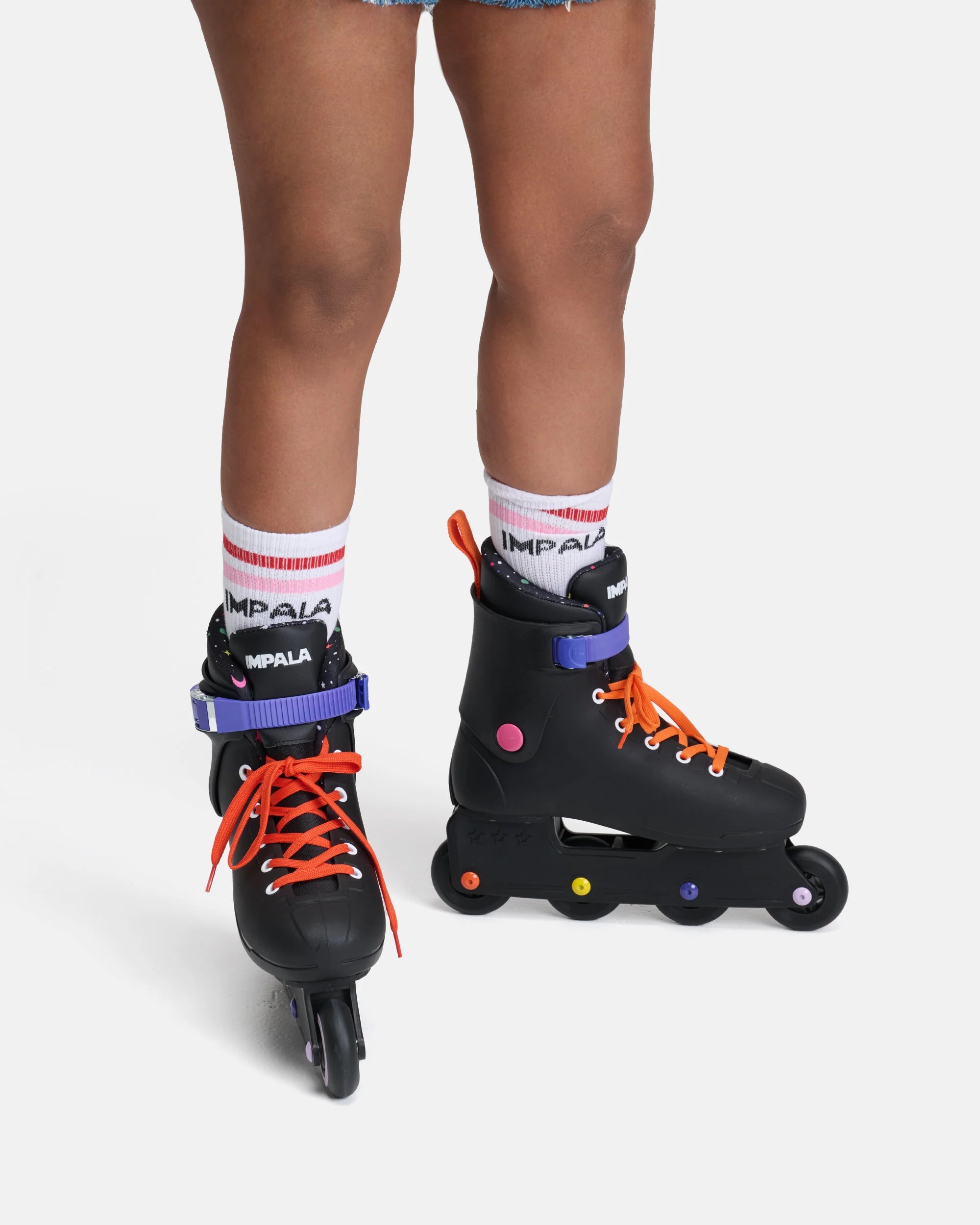 Black inline skates on legs with orange laces, purple cuffs, and multicolor wheels