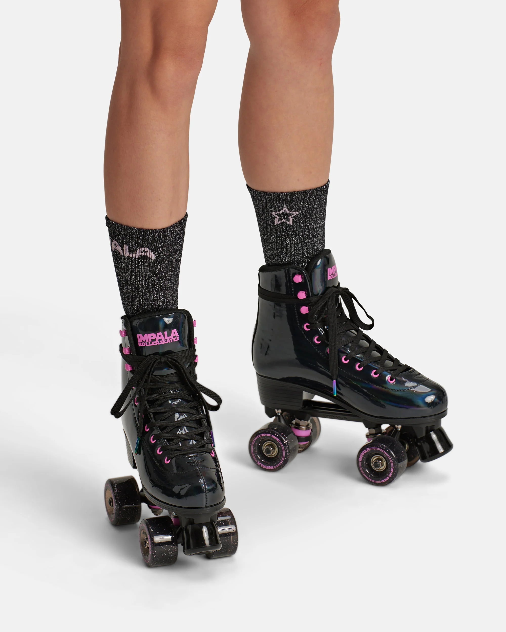 Pair of black quad skates with pink laces and glitter wheels, worn with socks