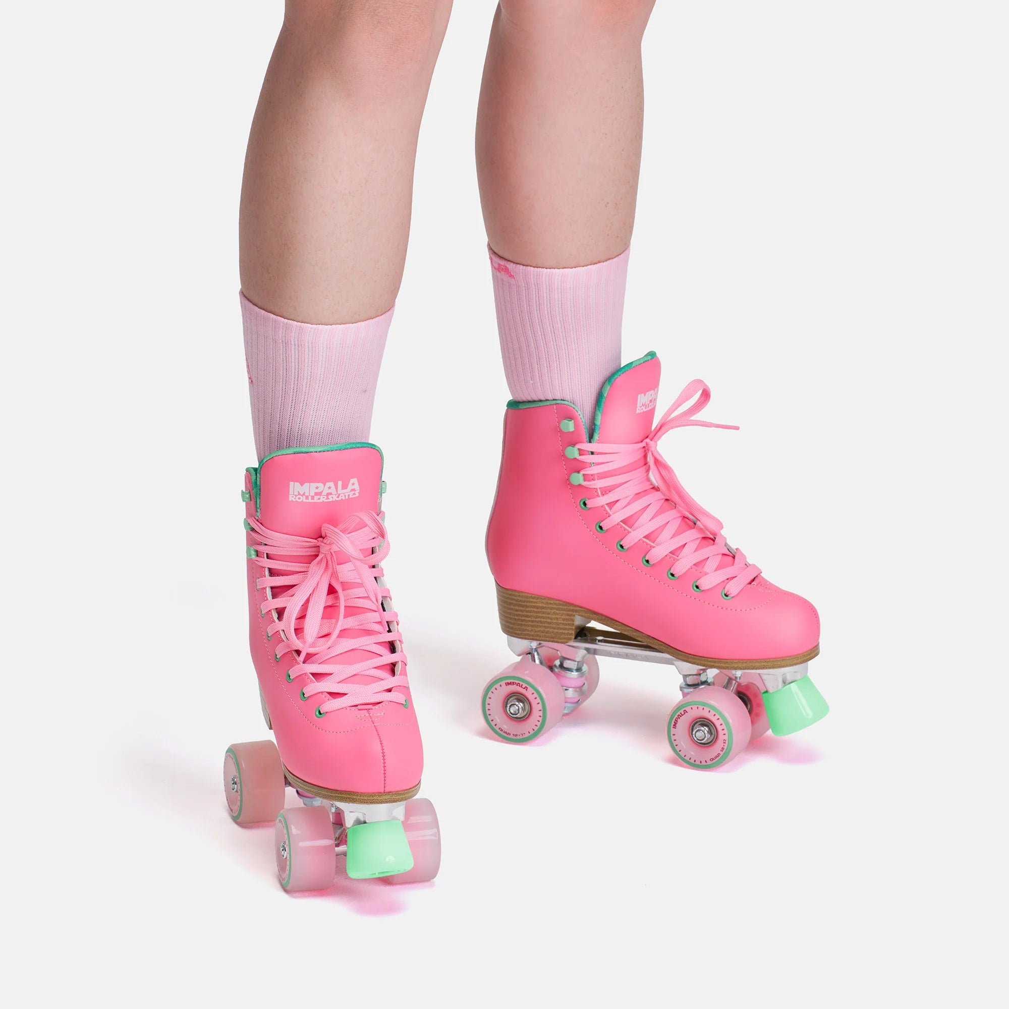 Pink quad skates on feet with green accent hardware, pink laces, and light wheels