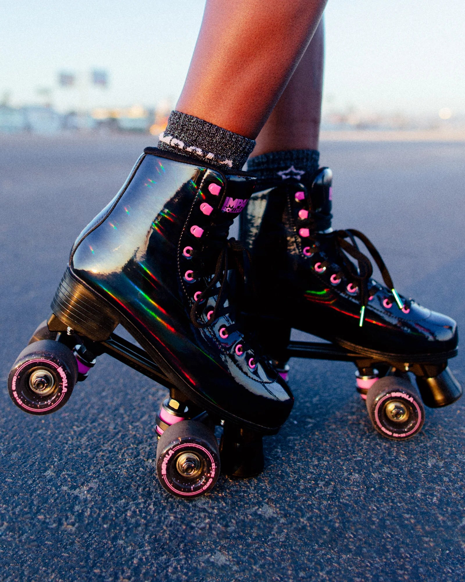 Black holographic quad skates with neon laces and pink glitter wheels on pavement