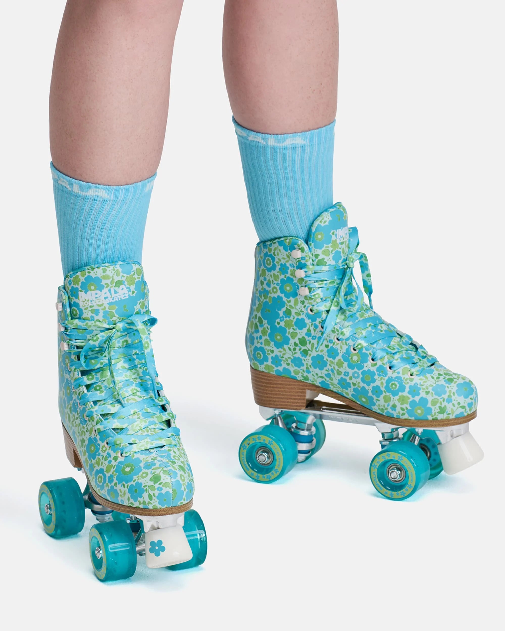 On-model teal floral quad skates with light blue socks and turquoise wheels