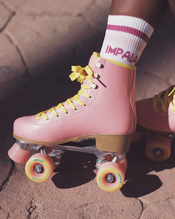 Pink Impala quad roller skates on pavement with yellow wheels and high-top fit