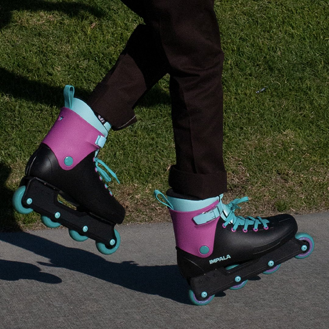 Inline skate on foot: black boot with magenta cuff, teal laces and teal wheels